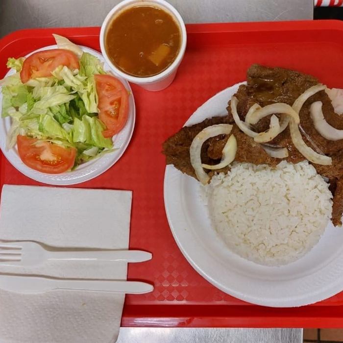 Plato de bistec encebollado con arroz blanco, vaso de habichuelas y ensalada de lechuga y tomate sobre bandeja roja