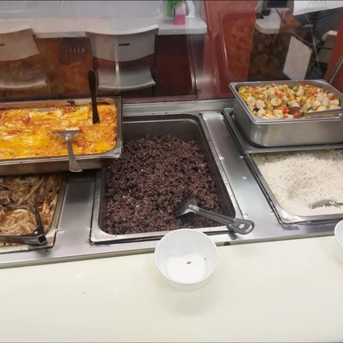 Mostrador caliente con bandejas de pastelón gratinado, pernil deshebrado, arroz moro, arroz blanco y vegetales mixtos