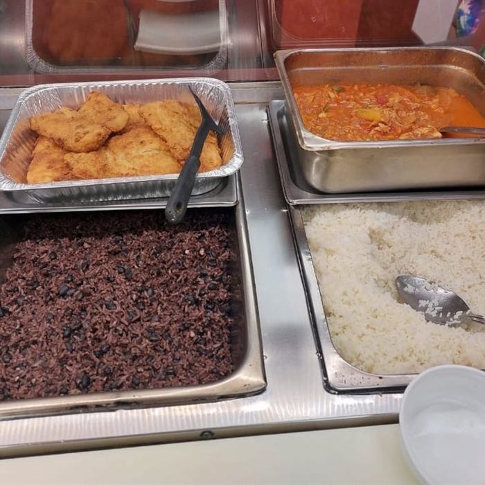 Mostrador caliente con bandejas de filetes empanizados, guiso con pimientos, arroz moro y arroz blanco