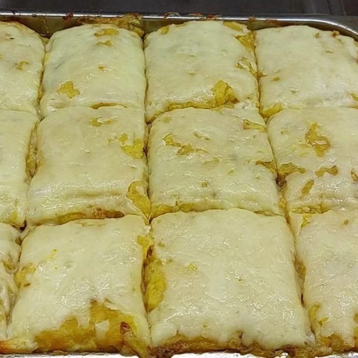Molde de aluminio con pastelón de amarillos cubierto de queso derretido, cortado en doce cuadros