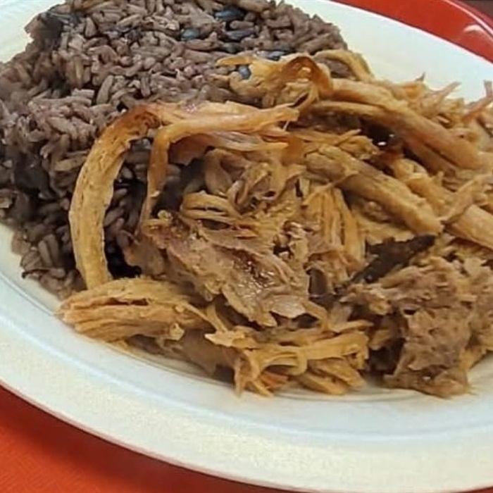 Plato de foam con arroz moro con habichuelas negras y pernil deshebrado, sobre bandeja plástica roja