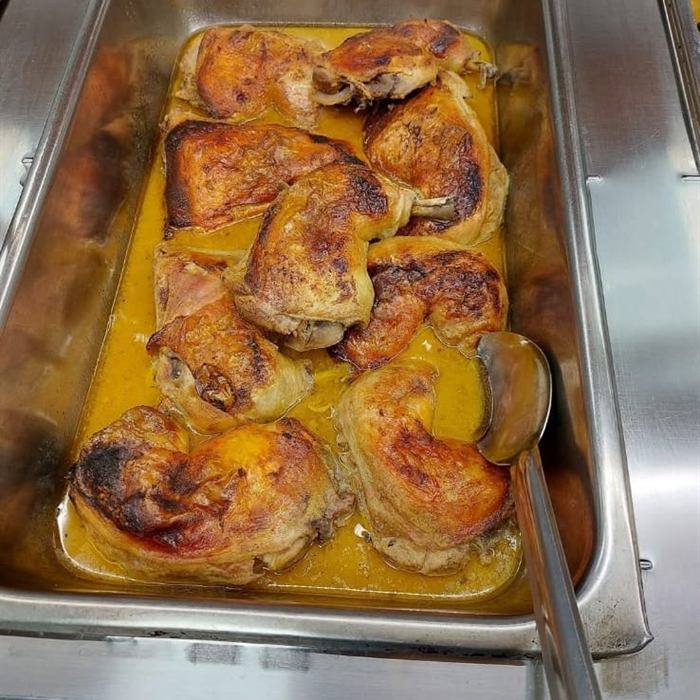 Bandeja de servicio con presas de pollo asado doradas reposando en salsa amarilla