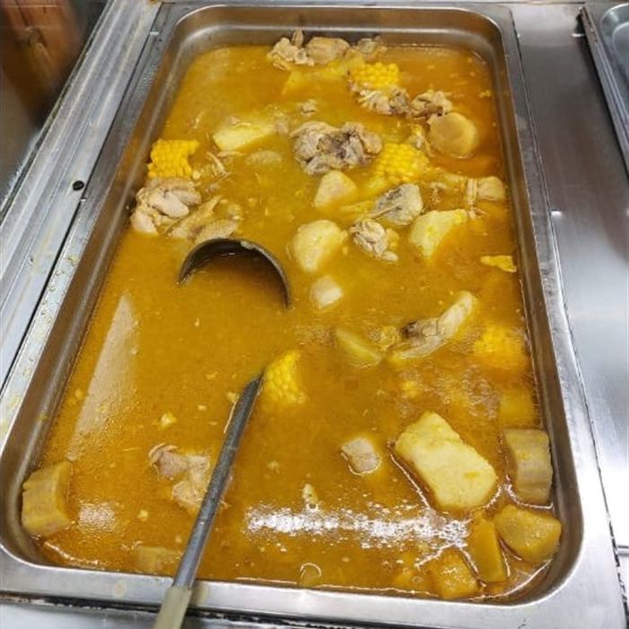 Bandeja de servicio con pollo guisado, mazorcas de maíz y trozos de papa en caldo anaranjado