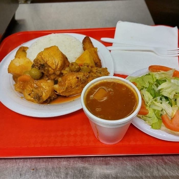 Plato de arroz blanco con pollo guisado y papas, vaso de habichuelas y ensalada de lechuga y tomate sobre bandeja roja